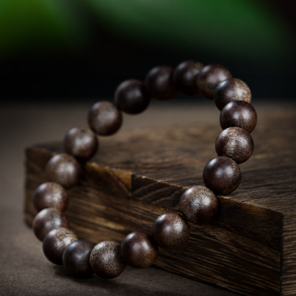 Dark brown agarwood bracelet at an angle on a wooden surface
