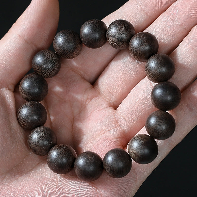 Dark brown wood bracelet held in a hand showing individual grain