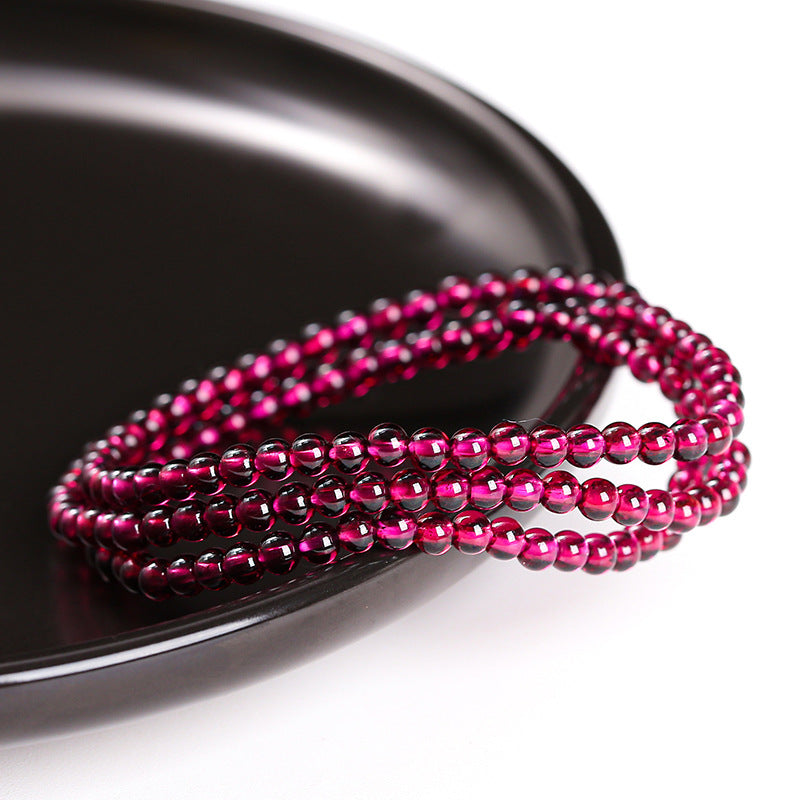 Wine-red garnet triple-wrap bracelet on a dark surface