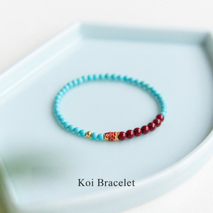 Turquoise-color and red koi bead bracelet shown on a tray