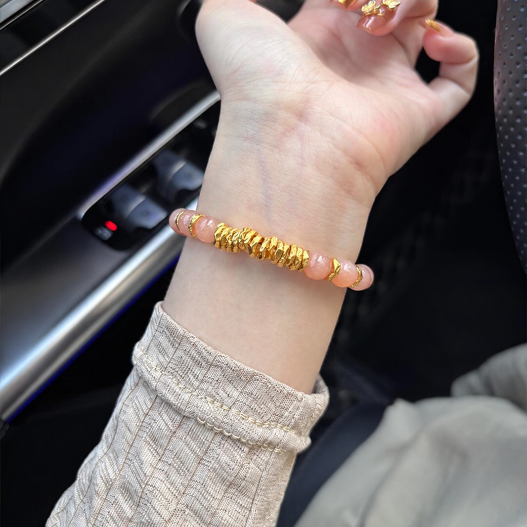 Pink sunstone bracelet with textured gold-tone disc accent worn on wrist