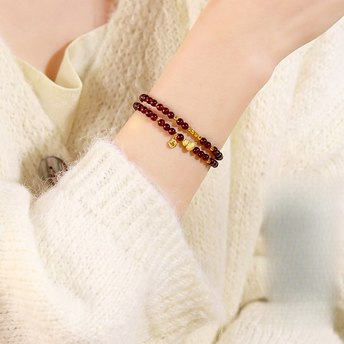Garnet double-wrap bracelet worn with a cream knit sleeve