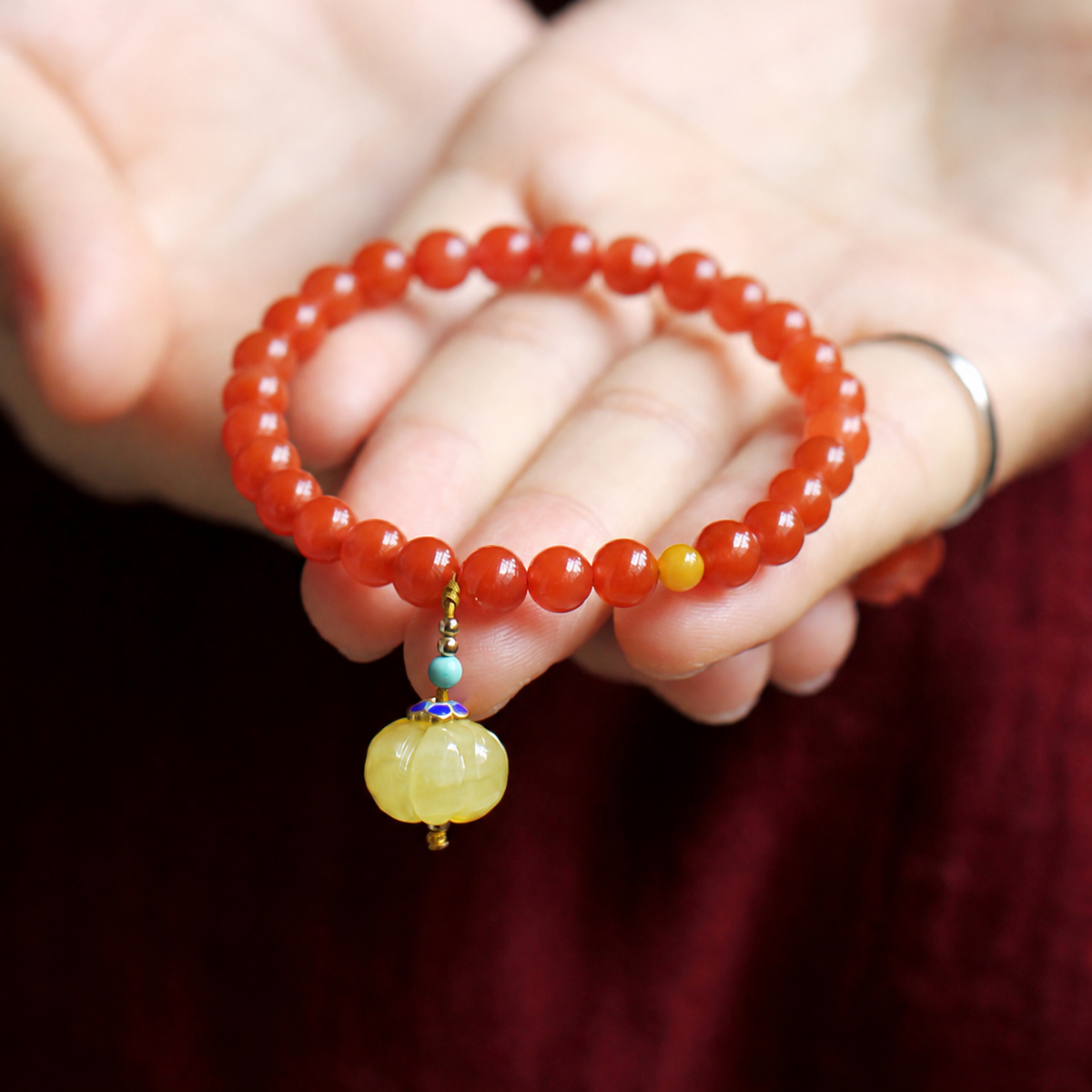 Nanhong red agate bracelet held to show its pumpkin pendant