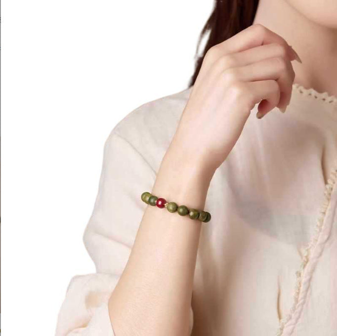 Green sandalwood and red accent bracelet worn on the wrist