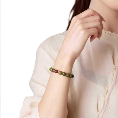 Green sandalwood and red accent bracelet worn on the wrist