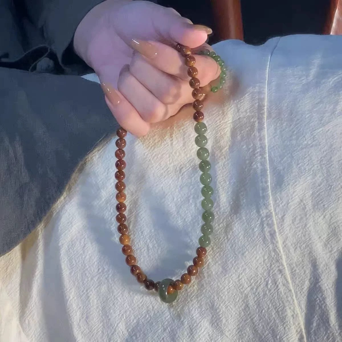 Long seed and jade bead strand with running ring held in hand