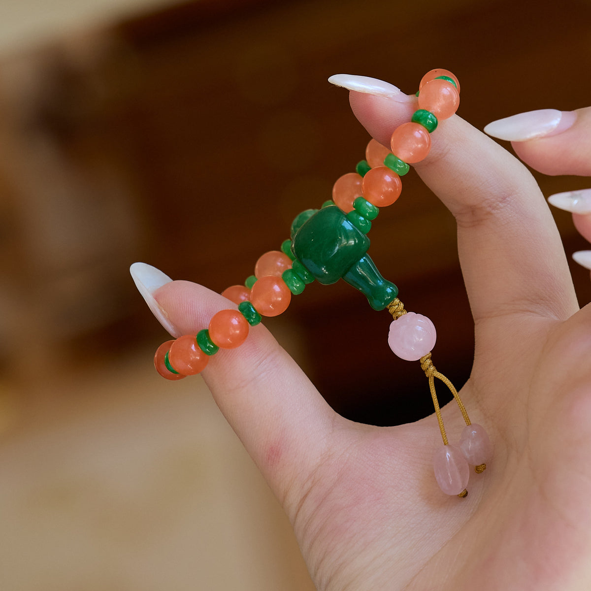 Orange bead bracelet with green accents held in a hand